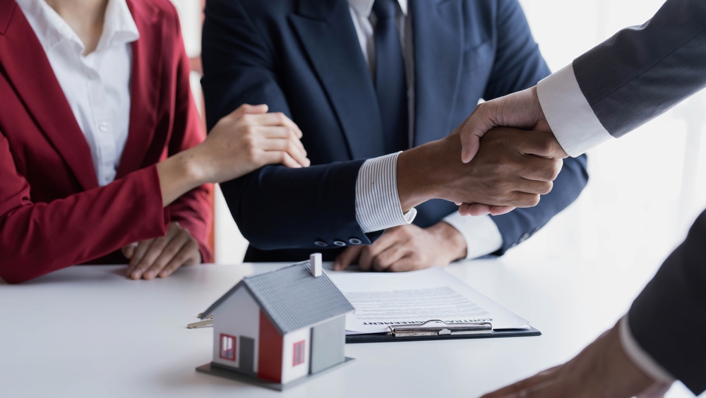 Business handshake over a real estate contract with a miniature house model.