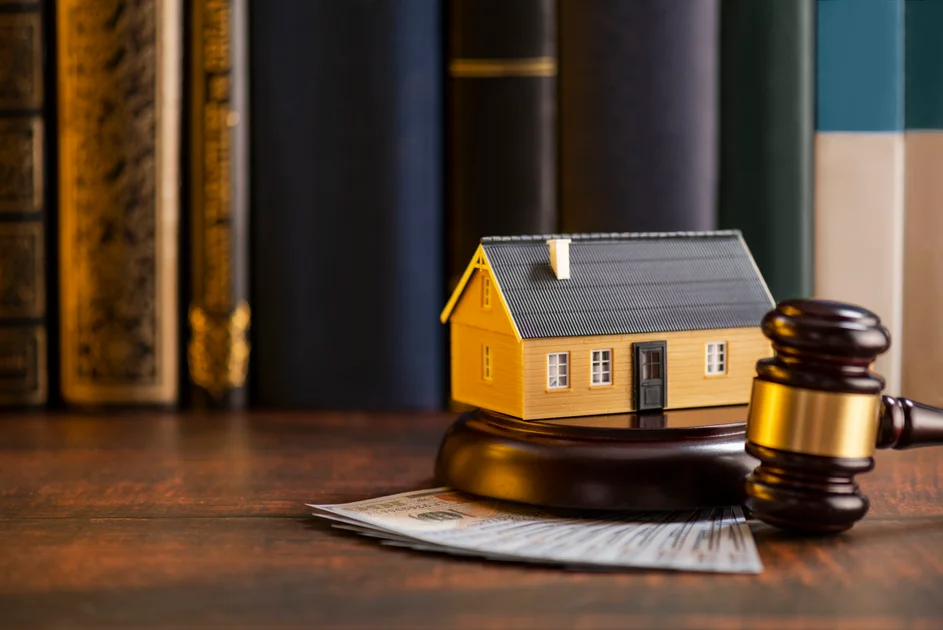 A miniature yellow house on a gavel with books in the background.